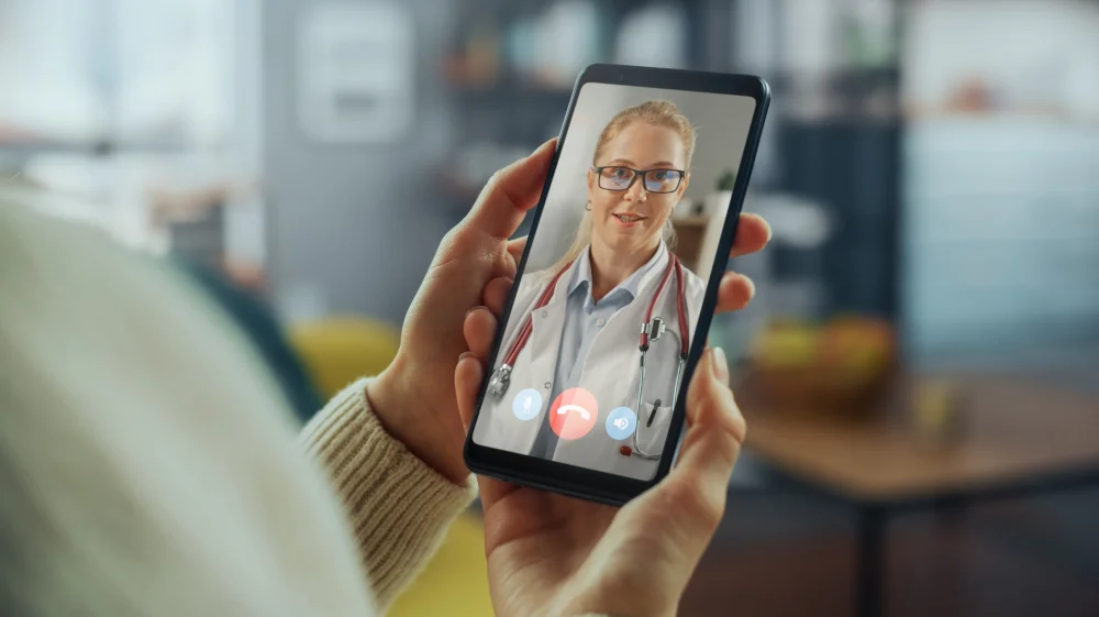 Wellness Telehealth Support A patient holding a smartphone during an active virtual telehealth video call with a wellness practitioner, highlighting home services offered by our Jupiter practice.